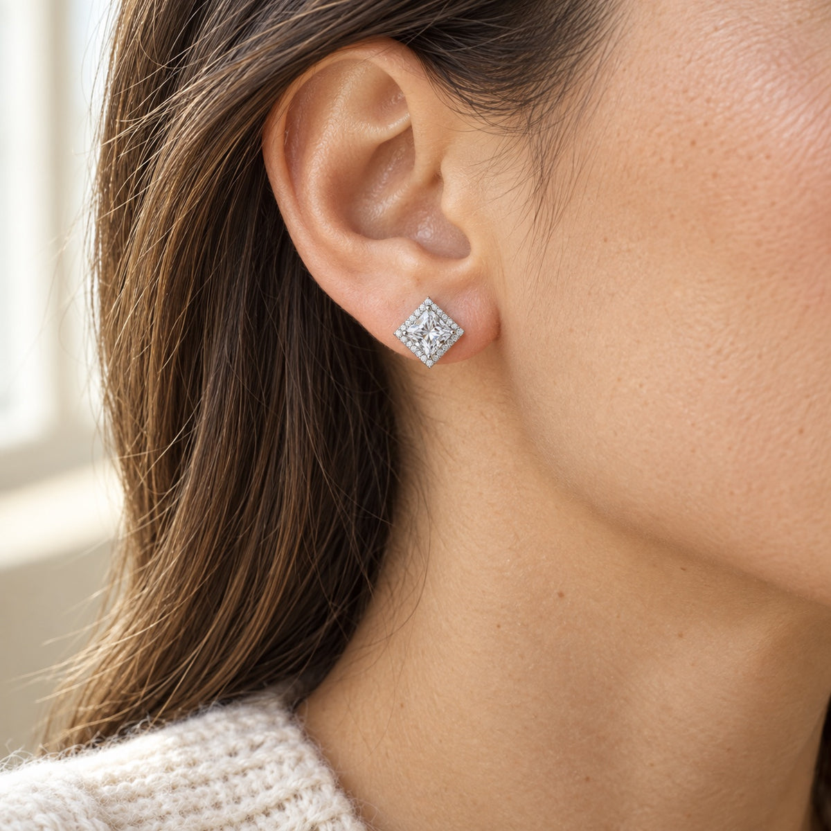 The Princess Halo Moissanite Studs worn by a model in natural daylight