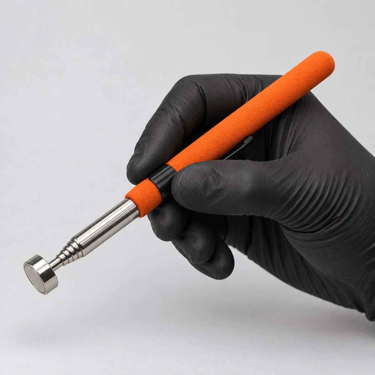 Telescopic magnetic pickup tool held in a gloved hand to show its size